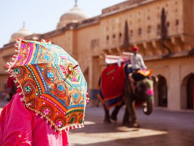 Rear view of woman holding colorful sun umbrella, Amber Fort, Jaipur, India. Indian elephants walking in the background.